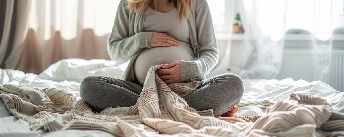 Schwangere Frau hält eine zusammengefaltete Krabbeldecke im Arm