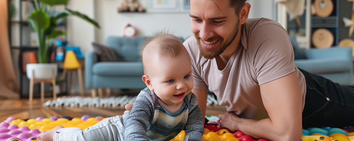Vater und Baby spielen gemeinsam auf einer Krabbeldecke im Wohnzimmer