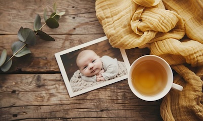 Geburtskarte mit Babyfoto liegt neben einer Tasse Tee und einer Musselindecke auf dem Tisch
